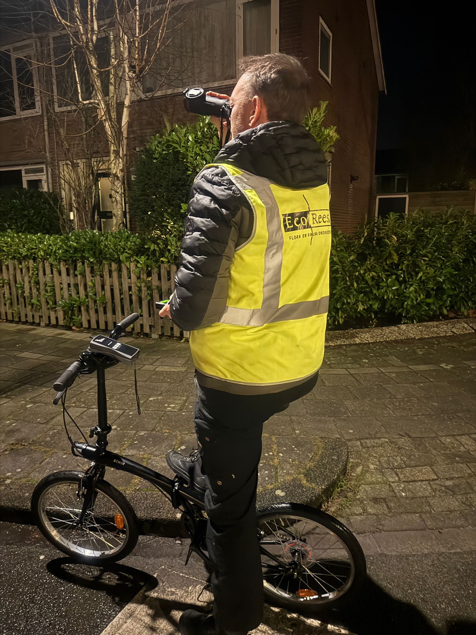 man op de fiets met geel hesje en verrekijker in zijn hand